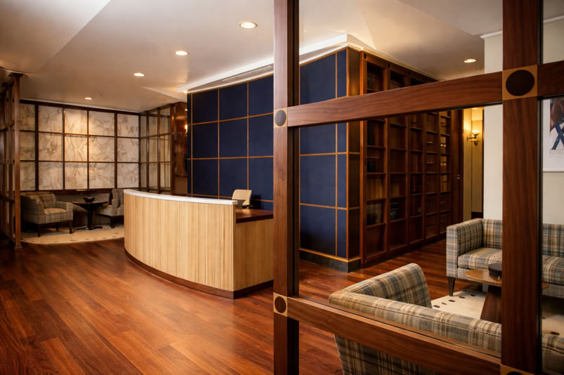 A modern reception area with a wooden desk, blue accent wall, wooden flooring, and seating area with plaid chairs.