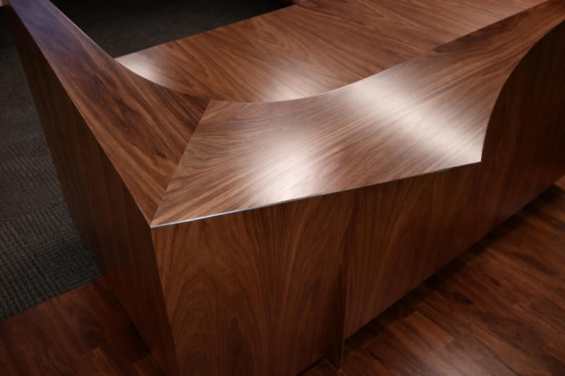 A wooden reception desk with a modern, angular design and a polished surface.