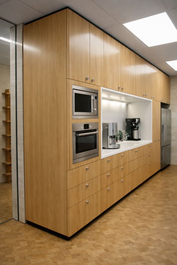 Wooden kitchen cabinets with built-in microwave, oven, and coffee machine, under bright ceiling lights.