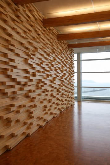 Wooden wall with a geometric pattern, wooden floor, and large windows with a view of the sky and landscape.
