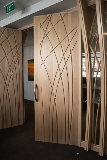 Wooden doors with abstract line patterns, partially open, revealing a room with a painting on the wall and a window.