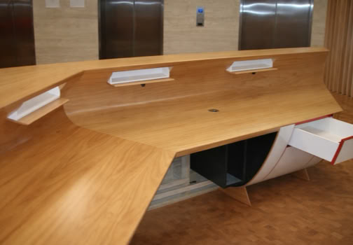 Curved wooden reception desk with open drawers, set in front of elevator doors.