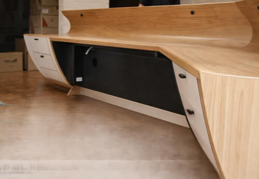 A modern wooden desk with curved edges and multiple drawers, set on a polished floor.