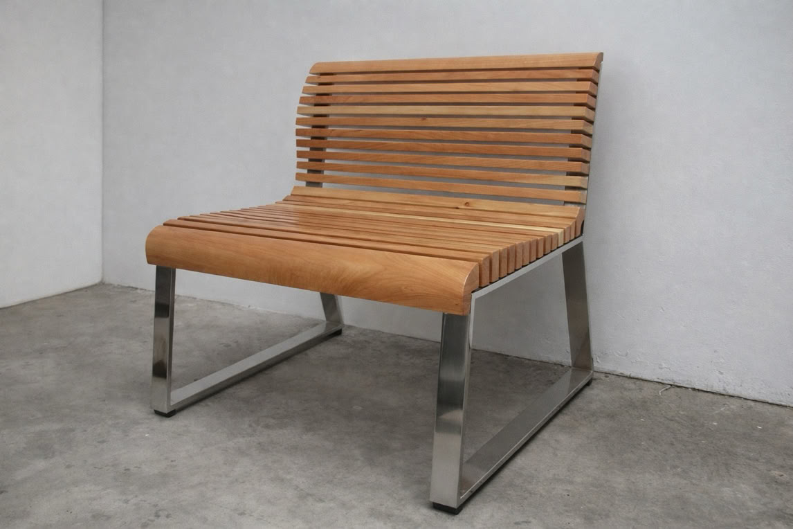 A wooden slatted chair with a metal frame, placed against a plain white wall on a concrete floor.