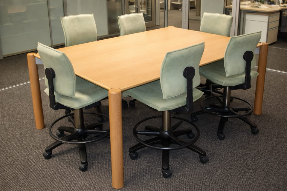 A wooden rectangular table surrounded by six light green swivel chairs on a carpeted floor.