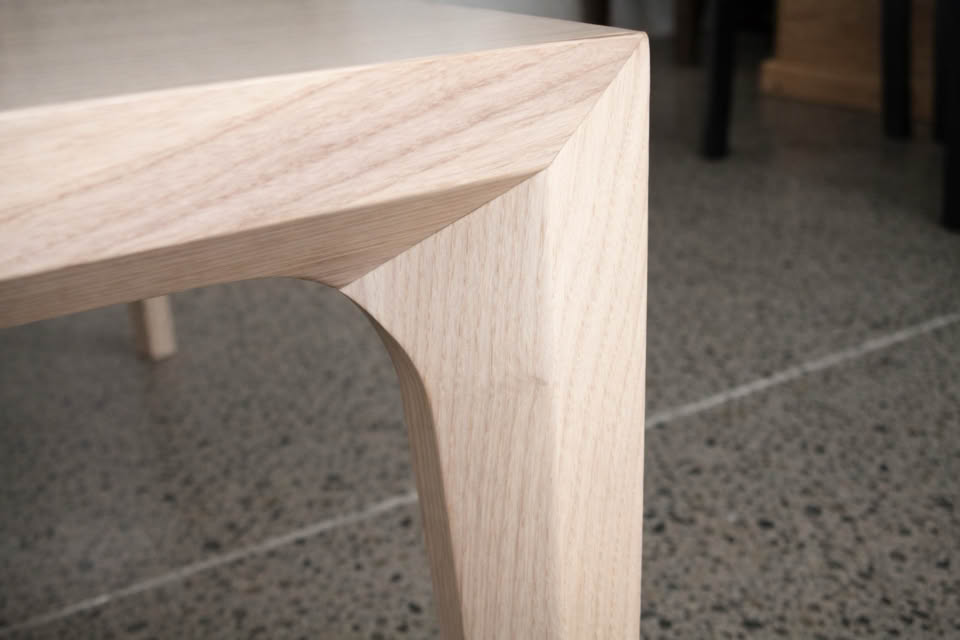 Corner of a wooden table with a smooth, angled design on a polished concrete floor.