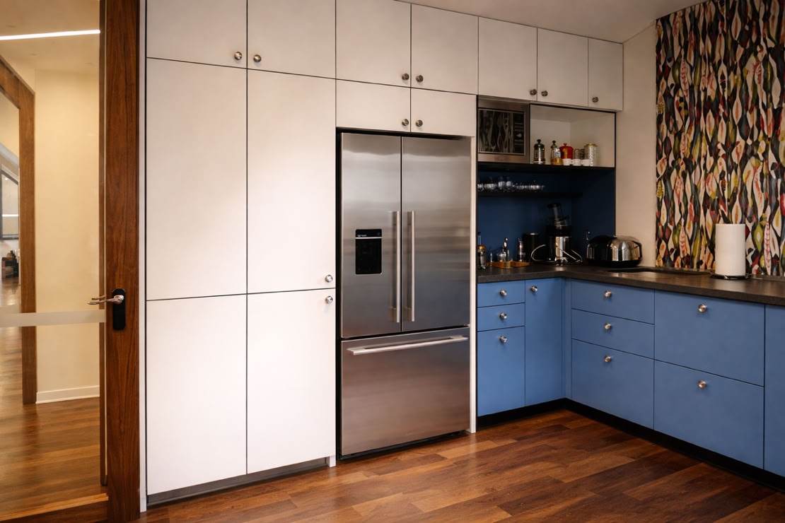 Modern kitchen with white upper cabinets, blue lower cabinets, a stainless steel refrigerator, and a colorful patterned wall.