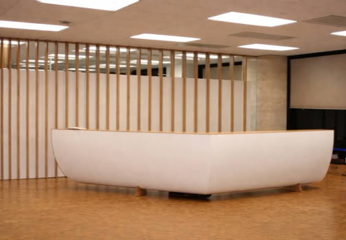 A modern reception desk with a curved design in a room with wooden flooring and vertical slat wall panels.