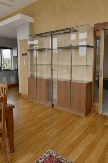 Wooden display cabinet with glass doors in a room with wooden flooring and a small rug in the foreground.