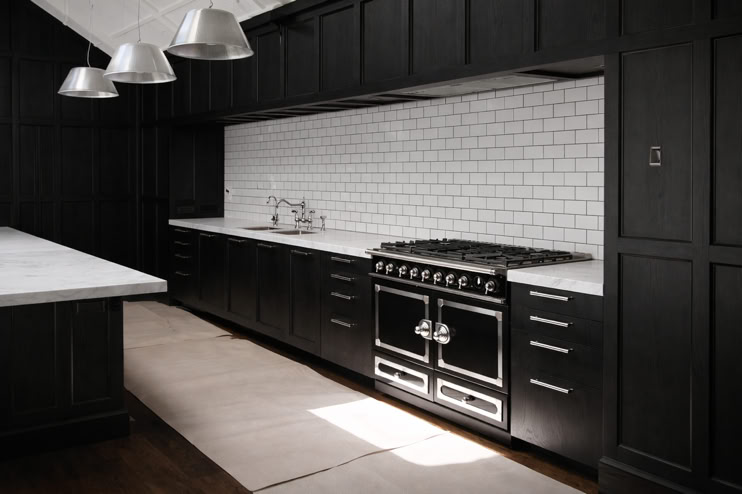 A modern kitchen with dark cabinets, a white subway tile backsplash, a large black oven, and three metallic pendant lights hanging above a white countertop.