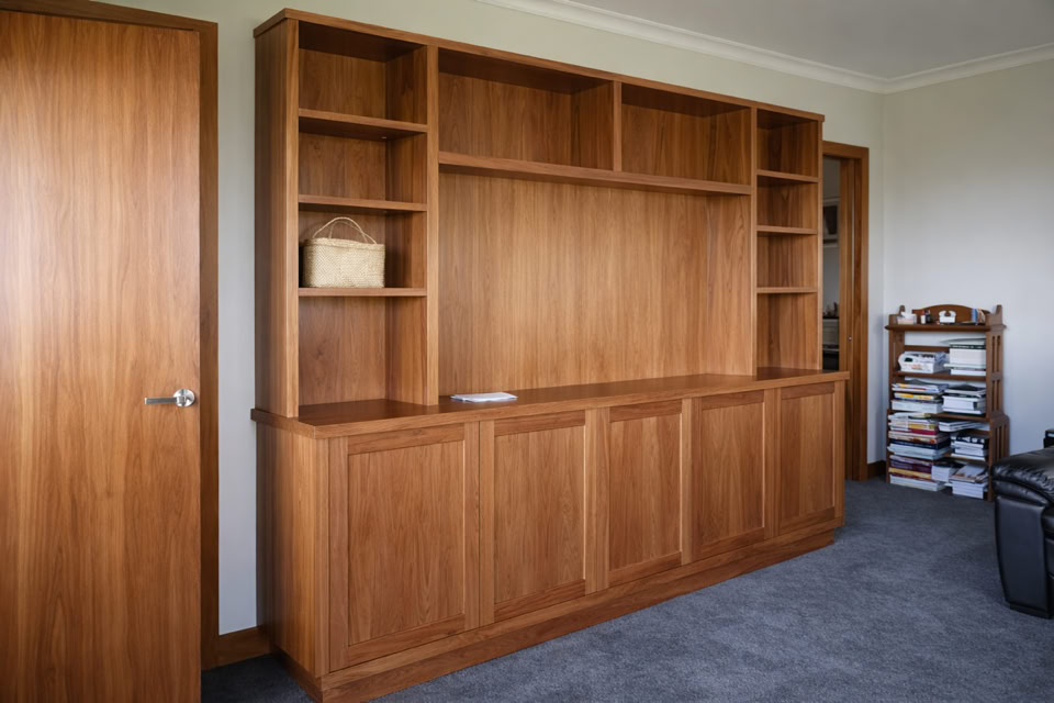 Wooden bookshelf with multiple shelves and cabinets, a door on the left, a small shelf with books on the right, and a carpeted floor.