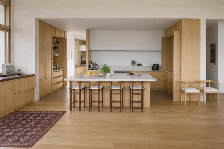 Modern kitchen with wooden cabinets, a large island with stools, and a rug on the wooden floor.