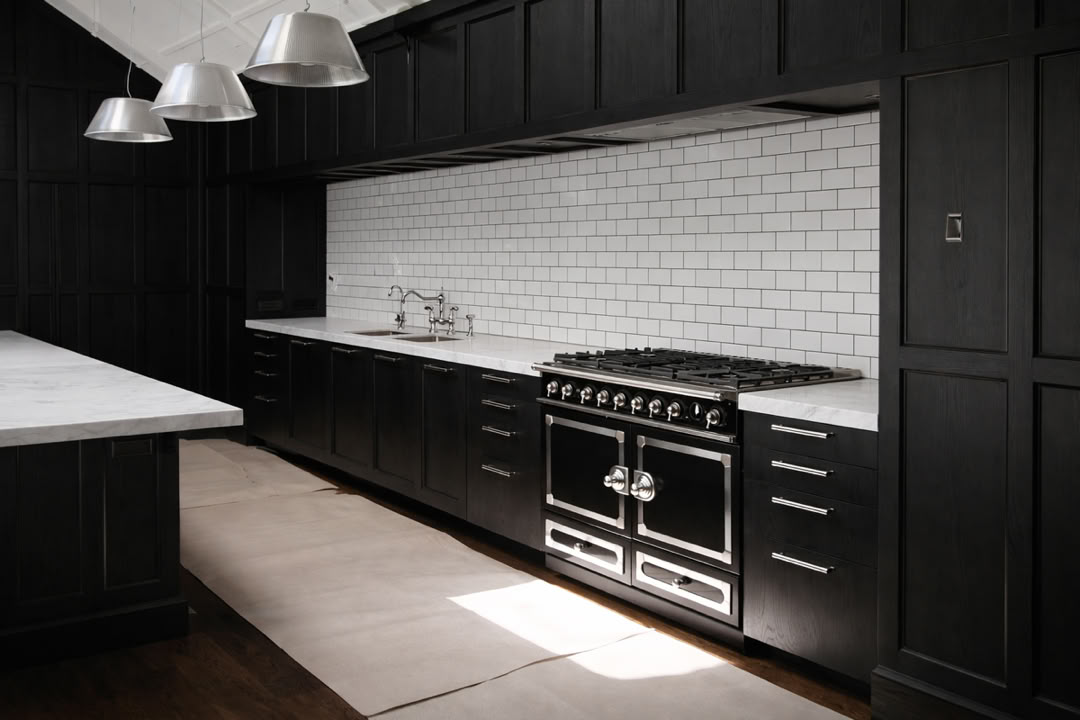A modern kitchen with dark cabinets, a white subway tile backsplash, a stainless steel stove, and three pendant lights hanging above a white countertop.